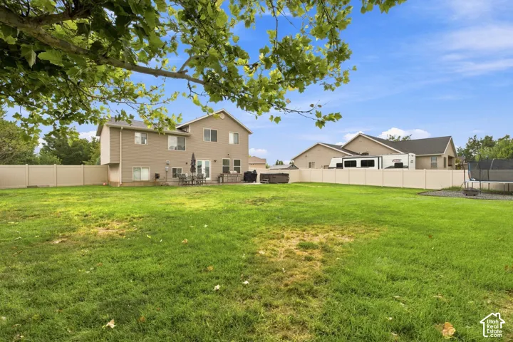 Expansive grassy yard with full perimeter fencing, patio space, and a built-in hot tub