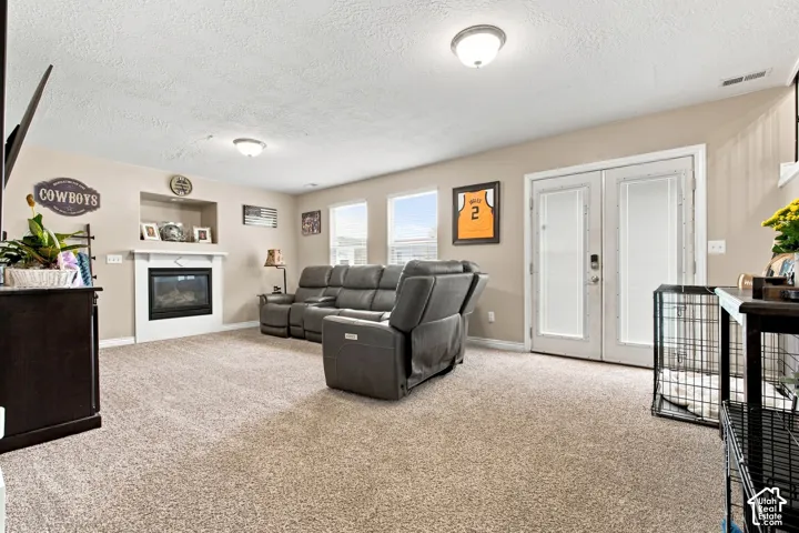 Recessed gas fireplace with a mantel, multiple windows, French doors with frosted glass, and neutral-toned carpeting
