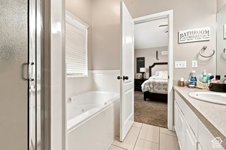 Master bathroom suite featuring a soaking tub with integrated shower enclosure, dual-sink vanity with quartz countertop, tile flooring, and direct access to the primary bedroom