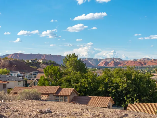 Terracotta roof tiles, stucco exteriors, and visible surrounding residential properties framed by distant red rock mountains
