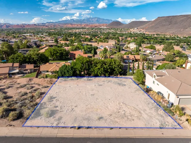 Expansive land parcel featuring a level building area, adjacent to a paved street, with surrounding residential properties and distant mountains