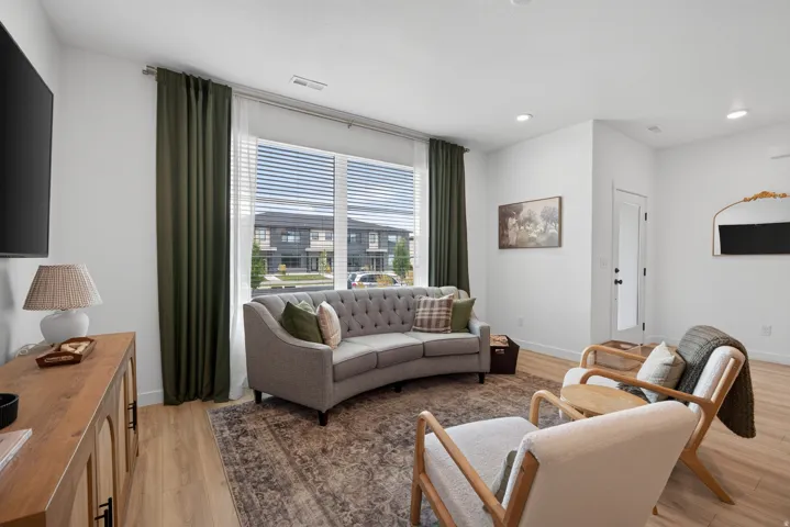 Main floor living room with sophisticated living room featuring expansive windows with motorized blinds and coordinating drapery, hardwood flooring throughout, a curved upholstered sofa, paired accent chairs with wooden frames, area rug, and recessed ceil
