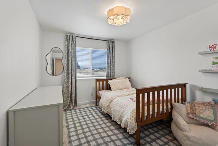 Second floor secondary bedroom with window with blinds, wall-mounted light fixture, and floating wall shelves.