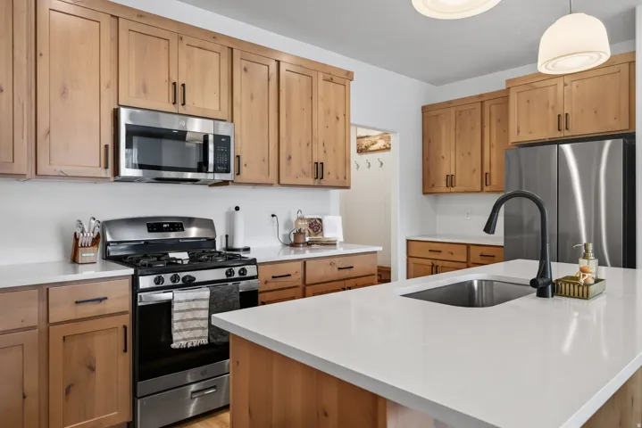 Main floor kitchen featuring wood cabinetry, stainless steel appliances, solid surface countertops, a gas range, and an undermount sink with a black matte faucet.