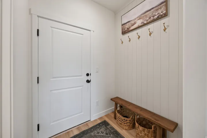 Main floor mud room with white paneled door with matte black hardware, wood-finish flooring, and white shiplap accent wall.