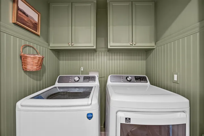 Second floor laundry space featuring beadboard paneling, two upper cabinets with brass-tone hardware, and painted crown molding.