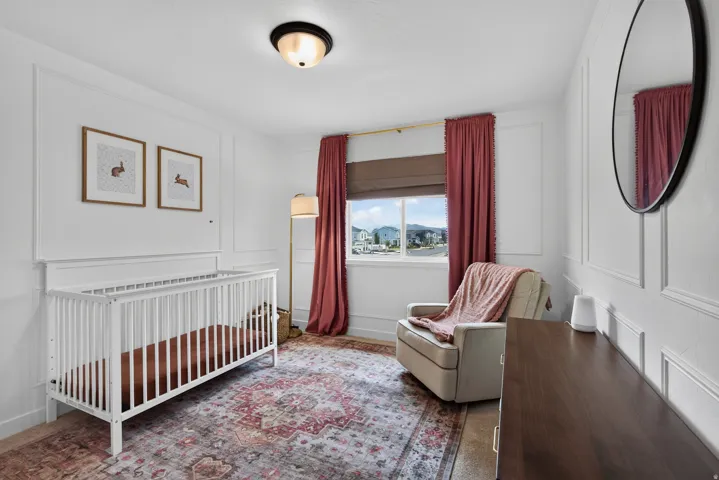 Second floor secondary bedroom with architectural wall paneling, flush mount ceiling light, and a window with roller shade.