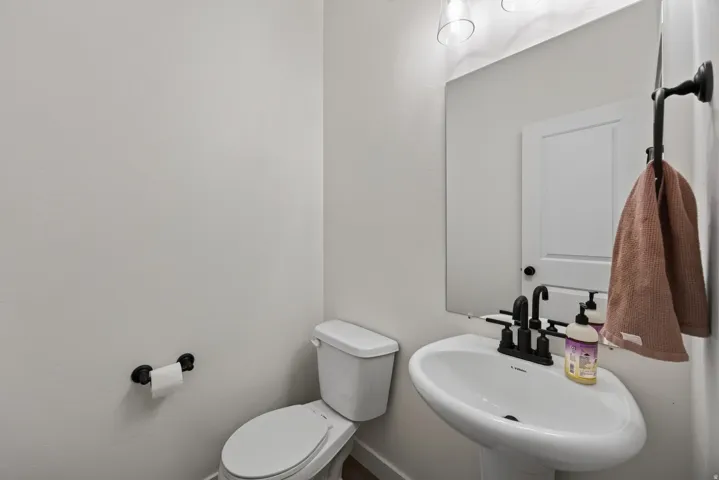 Main floor half bath with pedestal sink with black-finish faucet, wall-mounted mirror, and overhead vanity lighting.