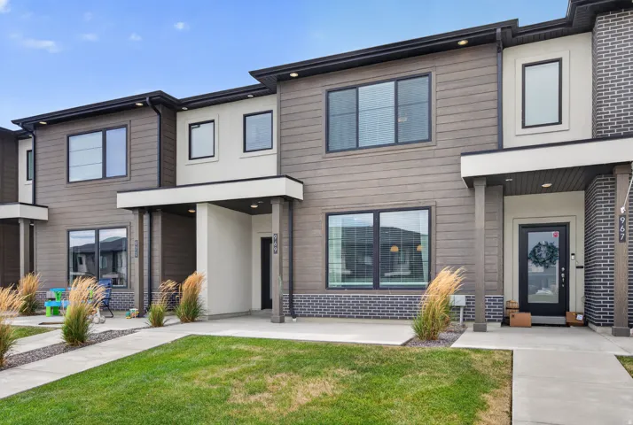 Contemporary townhome exterior featuring multi-toned siding, dark-framed windows, a covered entry, and a manicured lawn.