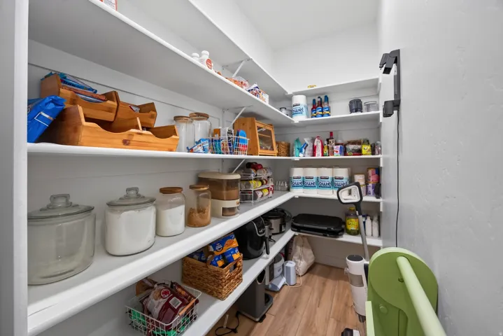 Main floor walk-in pantry featuring extensive built-in shelving, light wood-finish flooring, and light-toned wall paint.