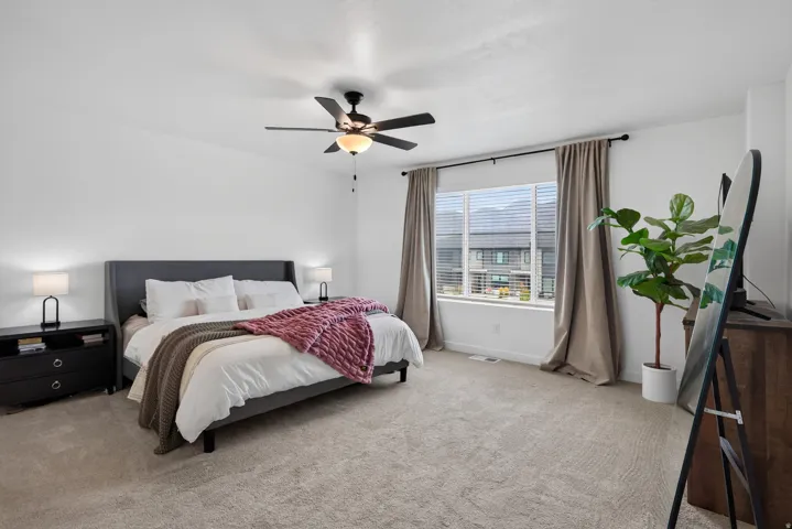 Second floor owners bedroom with carpeted flooring, ceiling fan with light fixture, large window with blinds, and neutral wall tones.