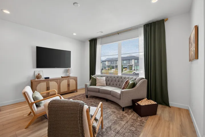 Main floor living room with recessed lighting, wood-finish flooring, large window with blinds, wall-mounted television.