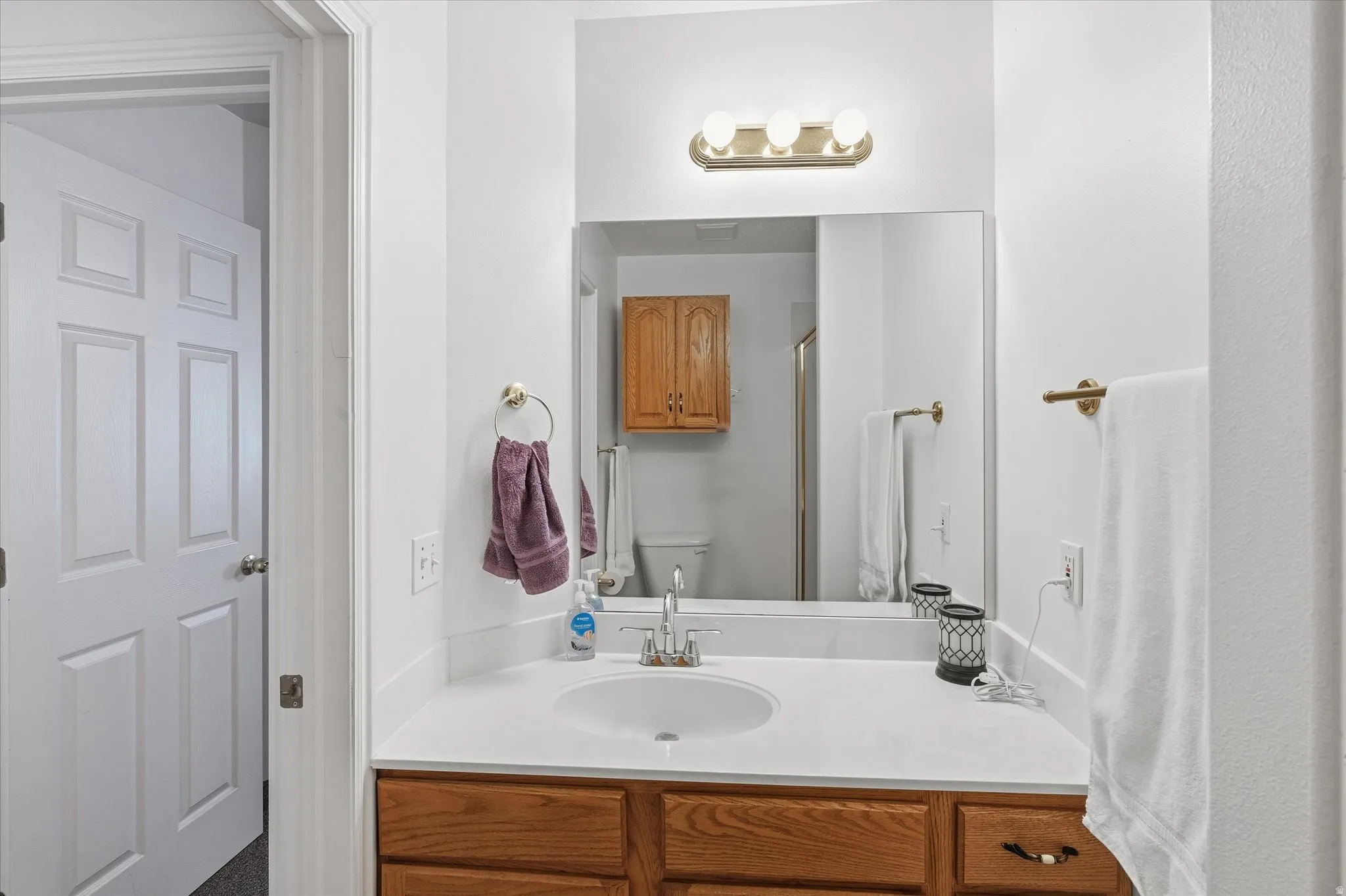 Vanity with wood-finish cabinetry, white countertop, and integrated sink