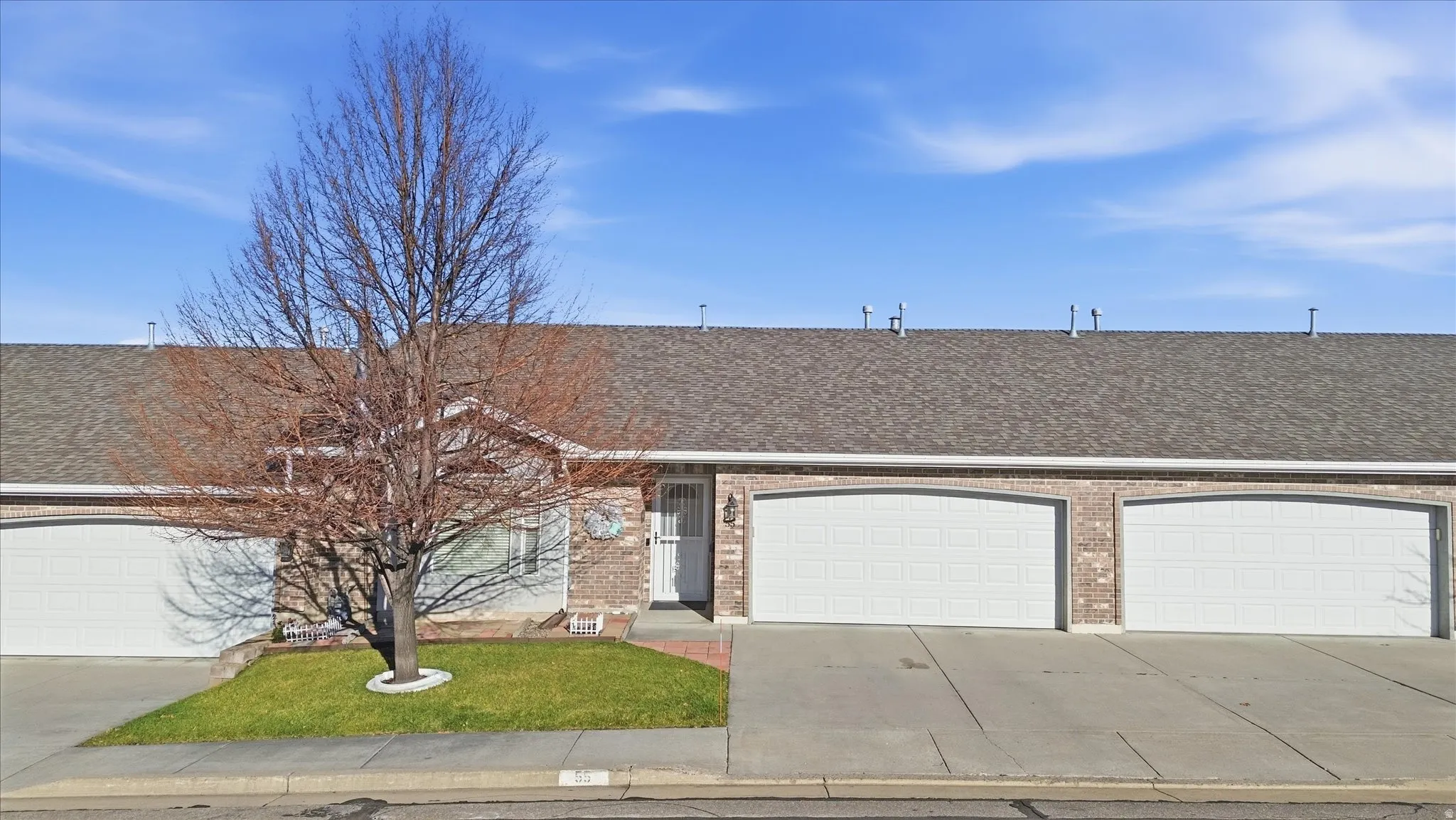 Brick exterior with multiple garage doors, a pitched shingle roof, and a mature tree