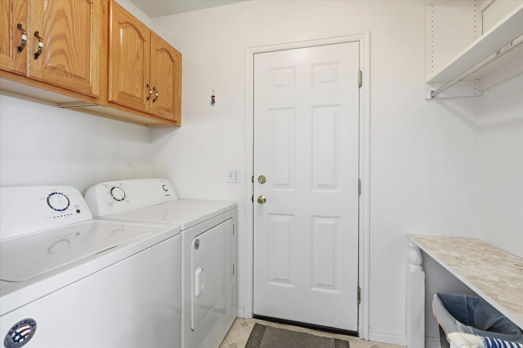 Laundry area featuring overhead wood cabinetry, a built-in folding counter, and wall-mounted shelving