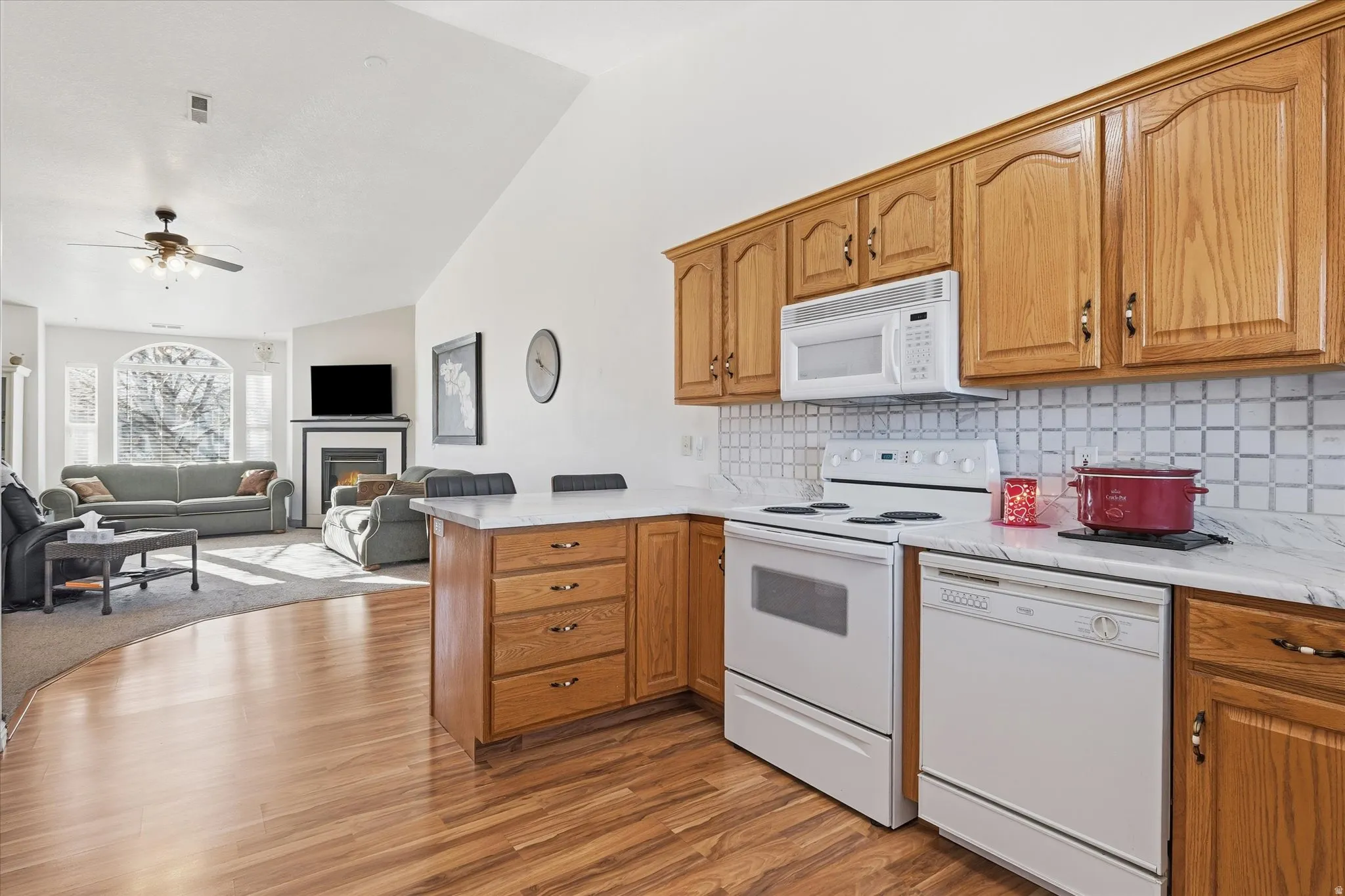 Vaulted ceilings, wood-finish flooring, fireplace with mantel, kitchen island with seating, and wood cabinetry