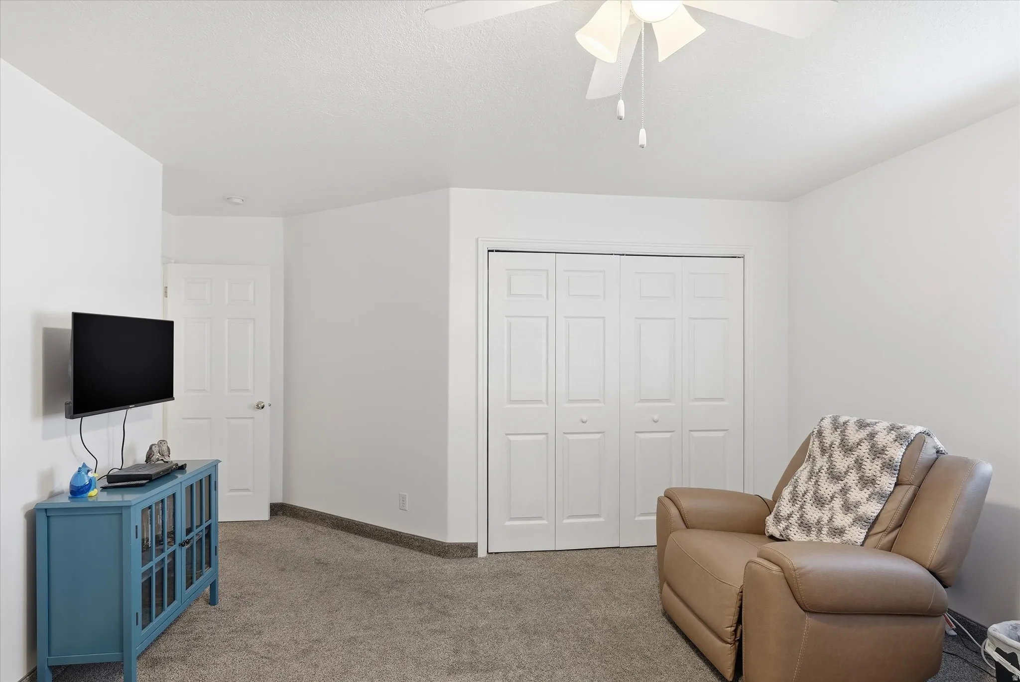 Neutral wall paint, textured ceiling, ceiling fan, carpeted flooring, and bi-fold closet doors