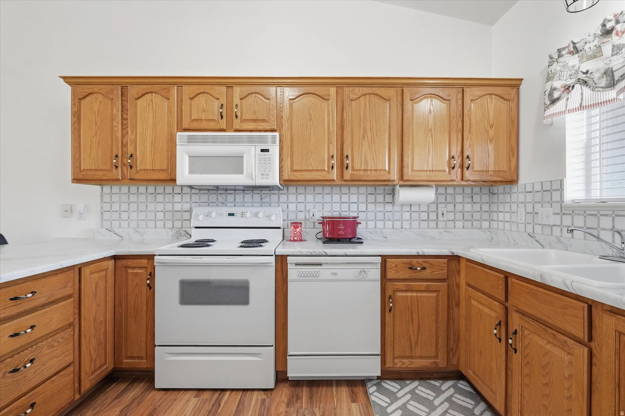 Kitchen featuring wood cabinetry, white appliances, white countertops, and a tiled backsplash