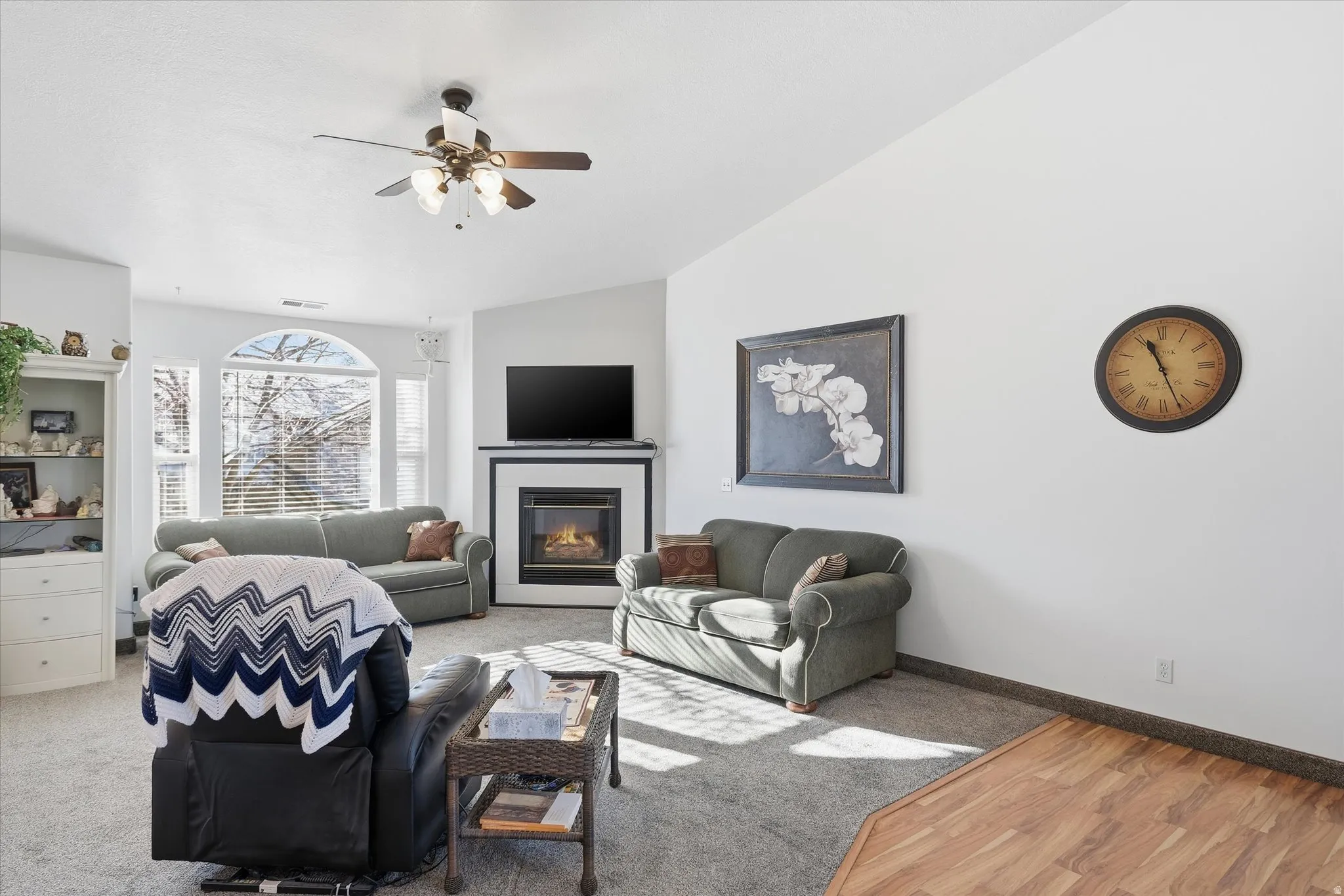 Vaulted ceiling with a ceiling fan, gas fireplace with mantel, arched window, wood-finish flooring, and built-in shelving