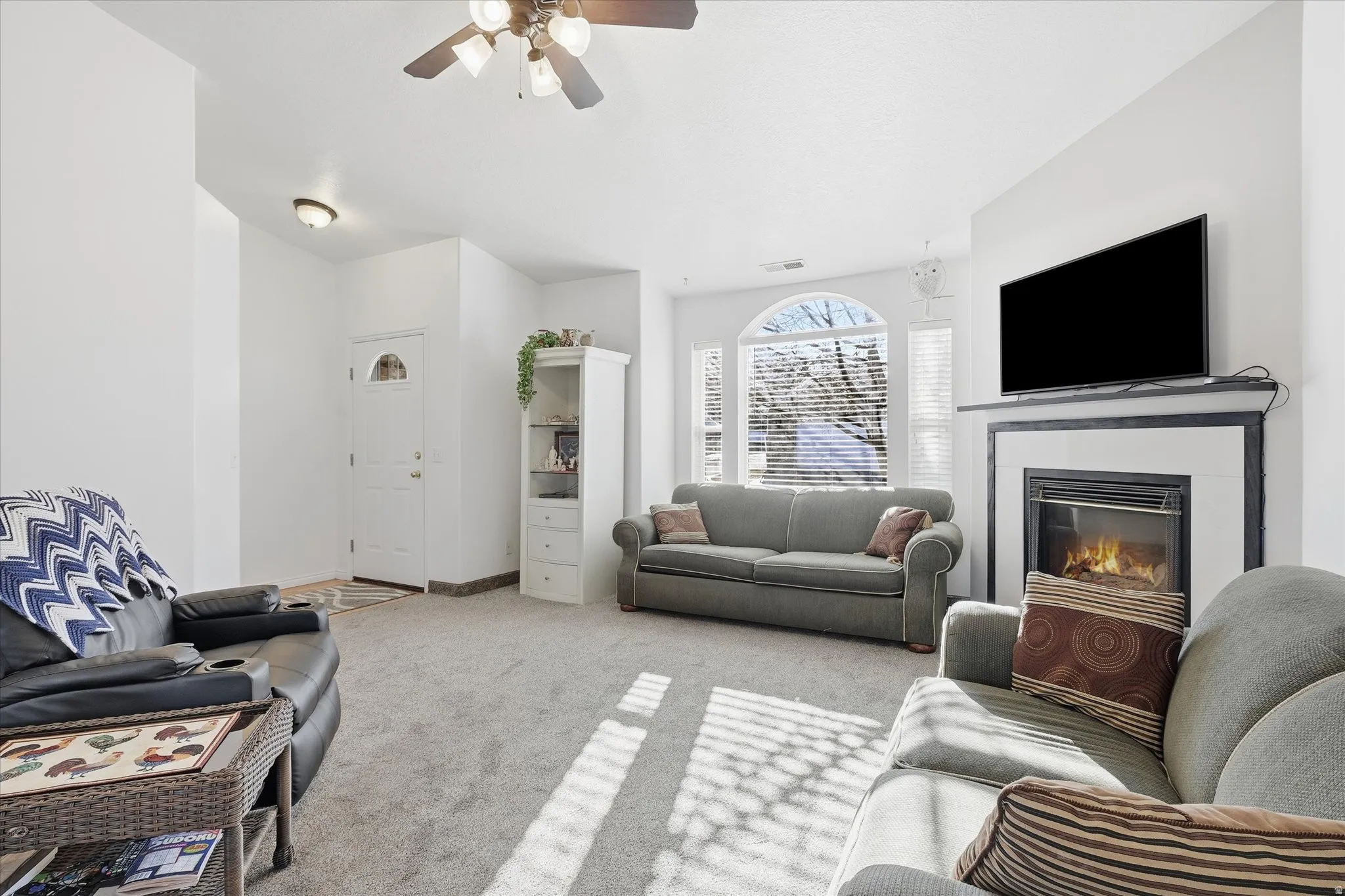 Living area featuring a fireplace with mantel, arched window, ceiling fan, and carpeted flooring