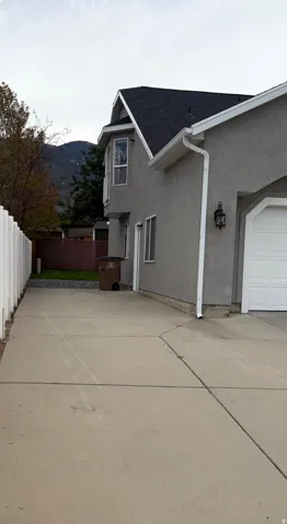 Stucco exterior with a bay window, concrete driveway, attached garage, and white fencing