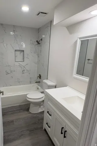 Bathroom featuring a white vanity with integrated sink, dark hardware, wood-finish flooring, and a tub with a tiled surround