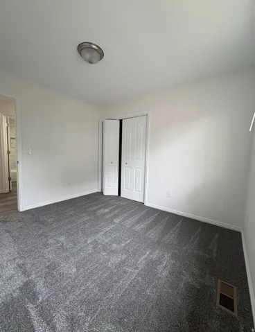 Neutral white walls, grey carpet flooring, white bi-fold closet doors, and an overhead flush-mount light fixture