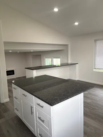 Modern kitchen island featuring a dark stone countertop, white cabinetry with multiple drawers and storage, and a secondary prep counter