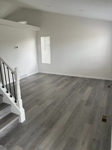 Vaulted ceiling, recessed lighting, wood-finish flooring, white painted walls, and a staircase with white balusters and black spindles