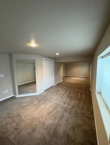 Spacious carpeted room featuring recessed lighting, bi-fold closet doors, a full-length wall mirror, and window blinds