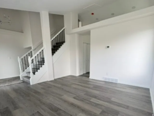 Wood-finish flooring throughout, recessed lighting, white walls, and a two-story staircase with dark metal balusters