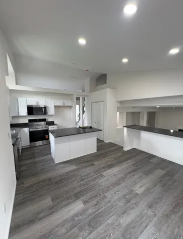 Open-concept kitchen with white cabinetry, stainless steel appliances, dark countertops, a central island, and wood-finish flooring