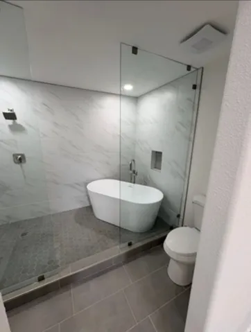 Frameless glass shower enclosure featuring a freestanding soaking tub, large format wall tiling, and hexagonal floor tiling