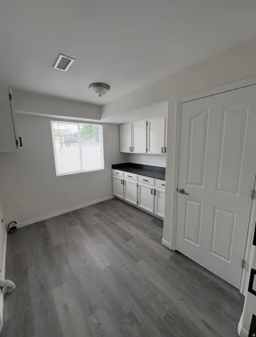 Wood-finish flooring, white cabinetry with black hardware, dark countertops, and a ceiling-mounted light fixture
