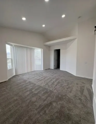 Spacious room featuring vaulted ceilings, recessed lighting, and bay windows with vertical blinds