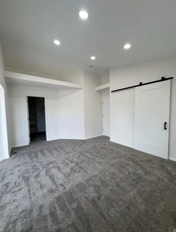 Recessed ceiling lighting, white walls, gray carpet flooring, and a modern barn door