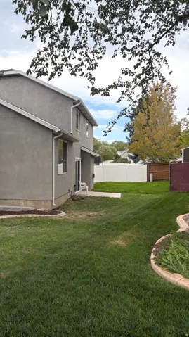 Stucco exterior with white trim, a concrete patio, and a spacious lawn bordered by decorative curbing