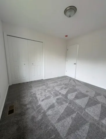 Spacious bedroom with geometric patterned carpet flooring, dual closet storage with white panel doors, recessed ceiling lighting, and neutral wall finishes