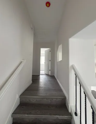 Staircase with wood-finish treads and risers, white handrails, and black wrought iron balusters