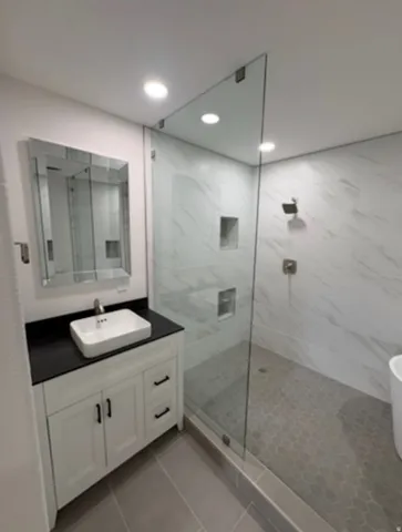 Modern bathroom featuring a frameless glass shower enclosure, white vanity with black countertop, vessel sink, and recessed lighting