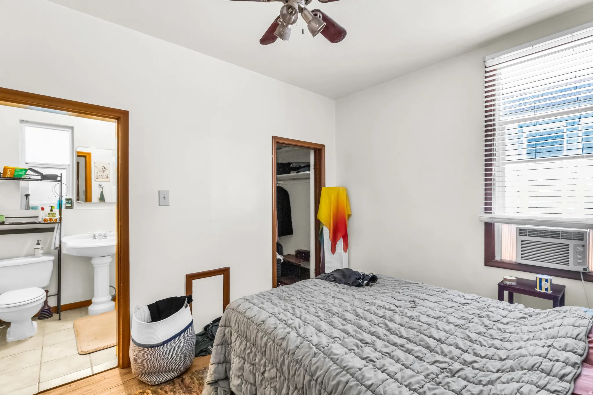 Hardwood flooring extending into the room from the doorway, window with blinds, ceiling fan, and a built-in air conditioning unit