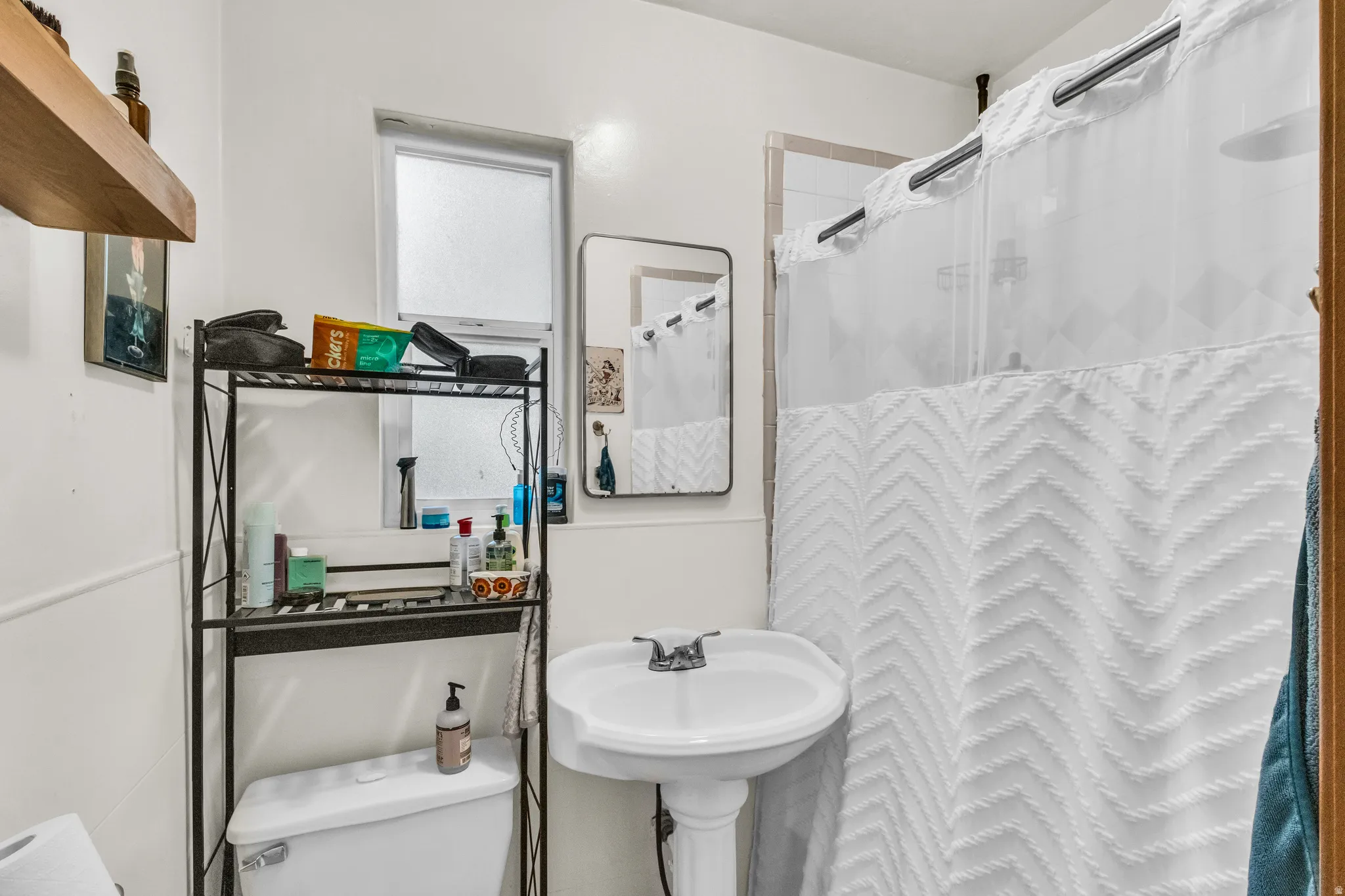 Pedestal sink with chrome faucet, built-in shelving, and a window with privacy glass