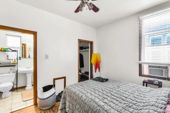 Hardwood flooring extending into the room from the doorway, window with blinds, ceiling fan, and a built-in air conditioning unit
