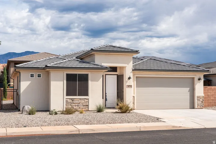 Stucco exterior with stone accents, tile roofing, an attached garage, and a gravel front yard