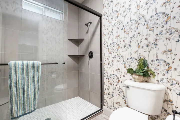Glass-enclosed shower with matte black fixtures, integrated shelving, and hexagon tile flooring