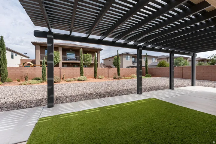 Expansive backyard featuring a pergola, concrete patio, artificial turf, gravel landscaping, and mature trees