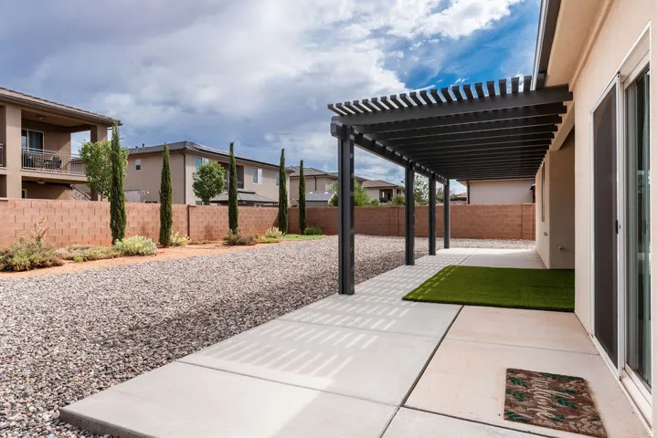 Expansive backyard featuring a full-length pergola, concrete patio, gravel landscaping, and a block privacy fence