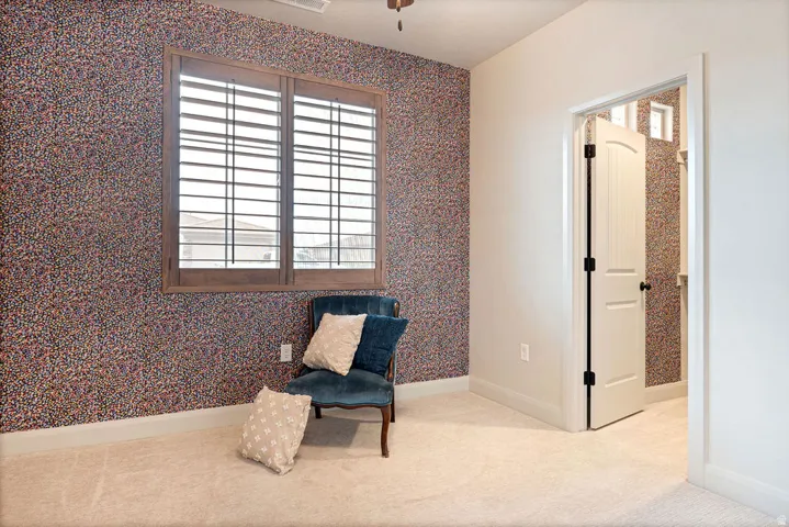 Textured wallpaper accent wall, wood-framed window with plantation shutters, neutral carpet, and white interior door with dark hardware