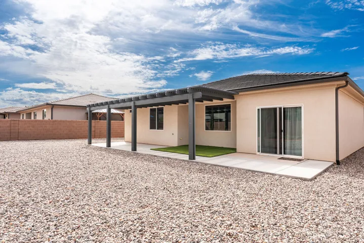 Stucco exterior with a covered patio featuring a pergola, sliding glass door, and a gravel yard