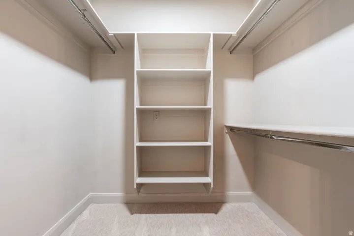 Spacious walk-in closet featuring built-in shelving, multiple hanging rods, and plush carpeting